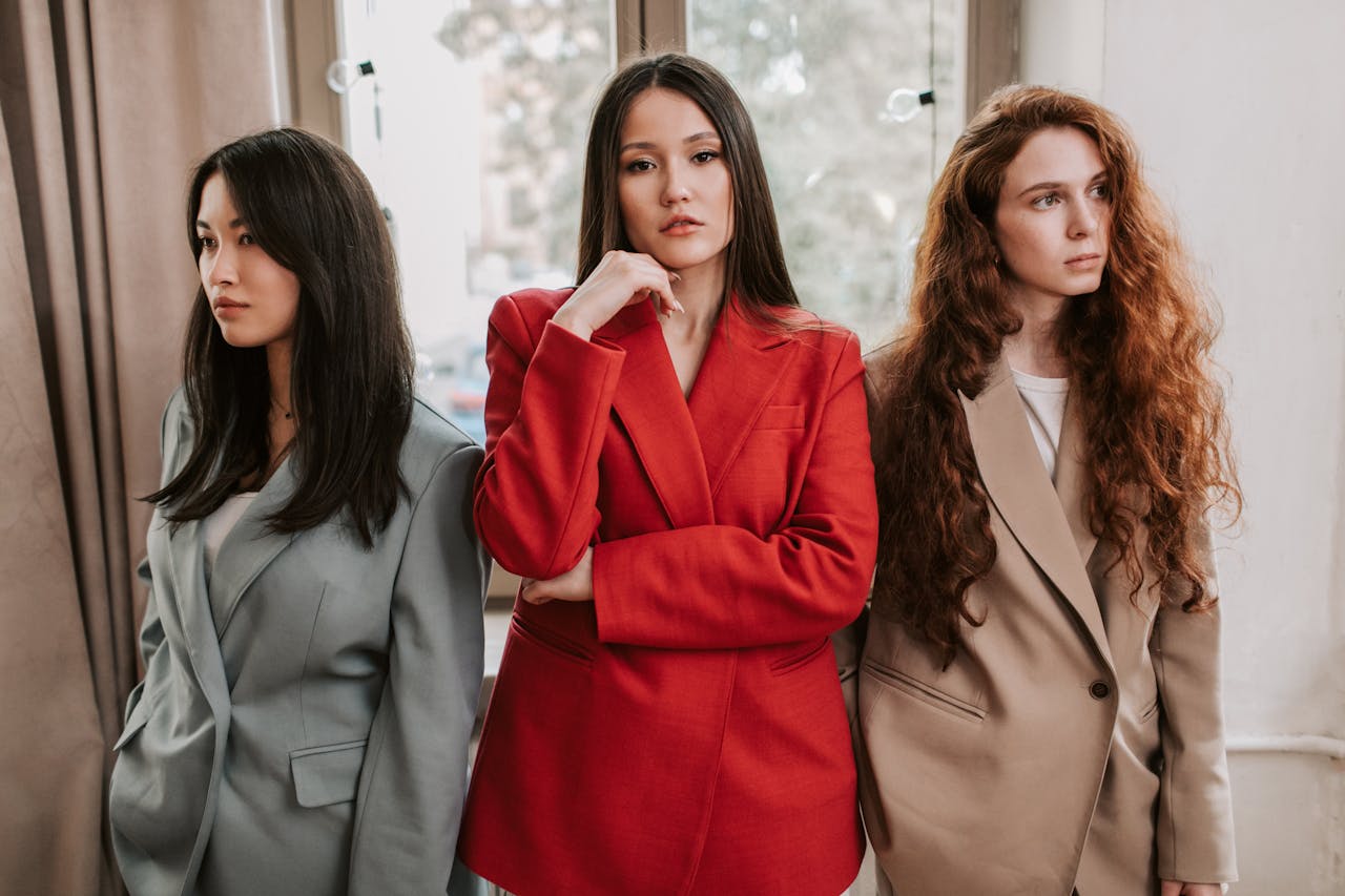 Three women in blazers posing with confidence, exuding modern fashion and style indoors.
