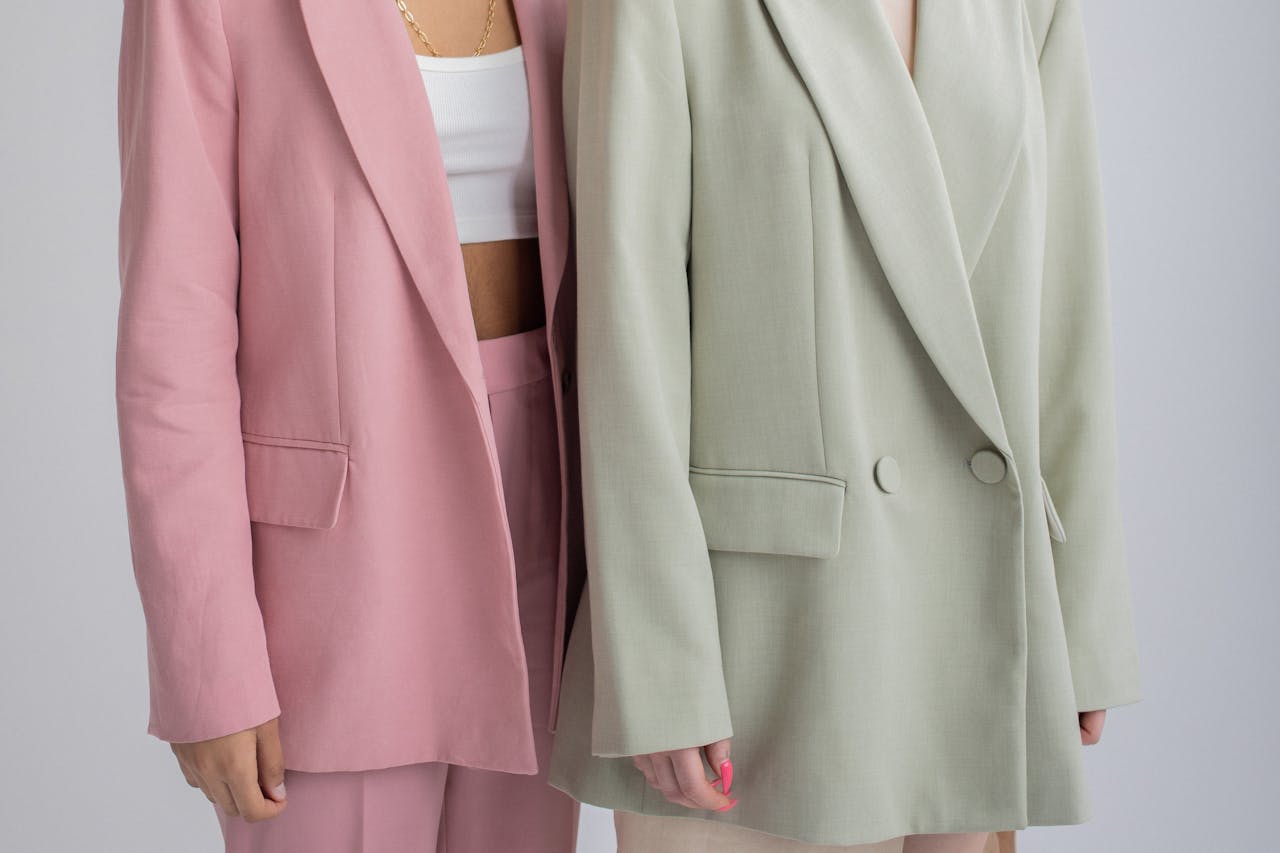 Crop unrecognizable female models wearing oversize stylish outfits standing close against gray background in studio